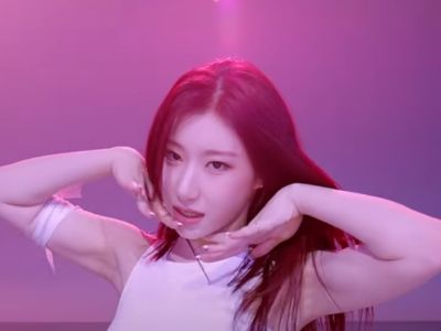 Chaeryeong is performing in a white dress under pink lighting.